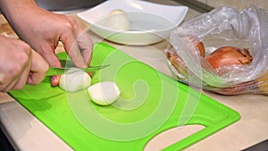 Person chops onion with knife on plastic cutting board closeup