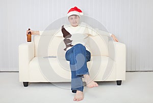 Person in a Christmas cap sits on sofa with beer