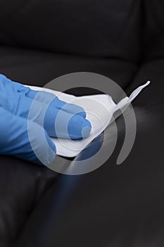 Person cleaning a brown leather sofa couch with a leather cleaner wipe.