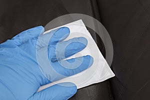 Person cleaning a brown leather sofa couch with a leather cleaner wipe.