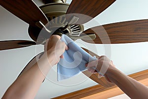 person cleaning ceiling fan blades with a microfiber cloth