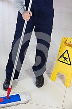 Person cleaning the floor with a flat mop near a yellow caution wet floor sign
