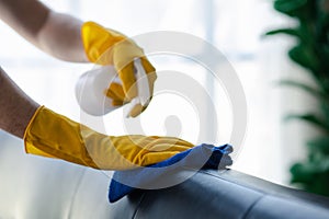Person cleaning the room, cleaning staff is using cloth and spraying disinfectant to wipe the sofas in the company office room.