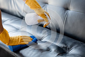 Person cleaning the room, cleaning staff is using cloth and spraying disinfectant to wipe the sofas in the company office room.