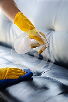 Person cleaning the room, cleaning staff is using cloth and spraying disinfectant to wipe the sofas in the company office room.