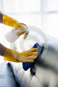 Person cleaning the room, cleaning staff is using cloth and spraying disinfectant to wipe the sofas in the company office room.