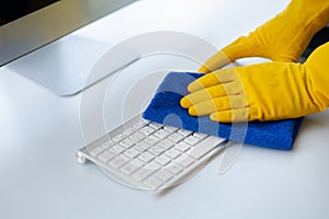 Person cleaning room, cleaning worker is using cloth to wipe computer keyboard in company office room. Cleaning staff. Concept of