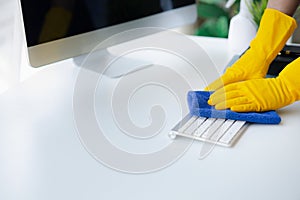 Person cleaning room, cleaning worker is using cloth to wipe computer keyboard in company office room. Cleaning staff. Concept of