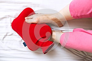 Person with cold feet in bed on a red hot water bottle