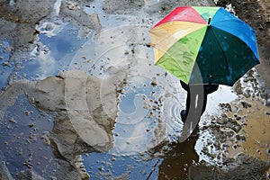 person with colorful umbrella standing by a large puddle