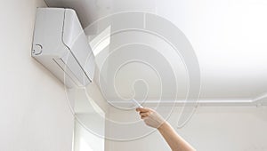 A person controls the air conditioner at home with a remote control. Split system for cooling the air and maintaining a