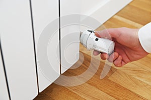 Person controls the heating.Hand adjusting thermostat valve of heating radiator in a room.