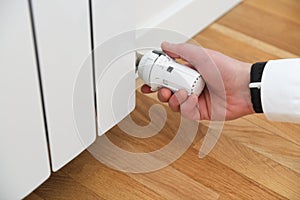 Person controls the heating.Hand adjusting thermostat valve of heating radiator in a room.