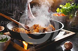 A person is cooking chicken in a pan on a stove