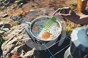 Person cooking fried eggs in nature camping outdoor, cooker prepare breakfast picnic on metal gas stove, tourism recreation