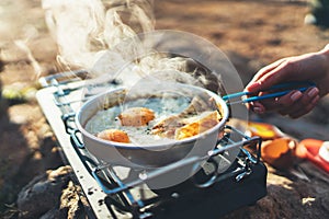 Person cooking fried eggs in nature camping outdoor, cooker prepare scrambled breakfast picnic on metal gas stove, tourism