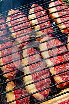 Person cooking raw steaks on a barbecue grill