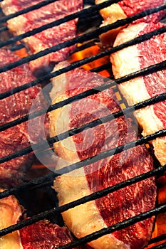 Person cooking raw steaks on a barbecue grill