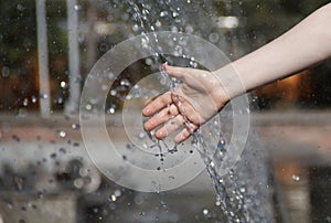 person cools his hands in the water jets of the fountain