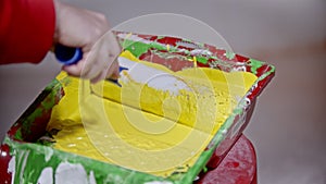 A person covering a roller in yellow paint in the paint tray