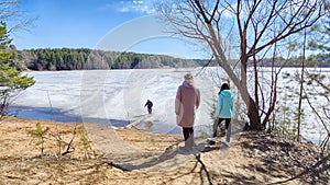 A person crosses a lake or river on old planks, logs, and branches. A dangerous crossing on melting ice in spring