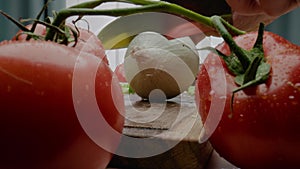 Person cuts off white onion tail on cutting board by tomato