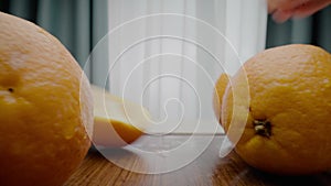 Person cuts orange into half lying on wooden cutting board