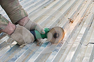 A person cuts a sheet of roofing iron with a special electric tool.Angle grinder for metal cutting. Sparks fly. Gloved hand.