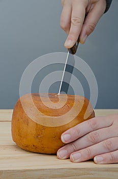 Person cutting with knife a slice of cheese wheel
