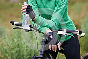 Person, cyclist and hands with water bottle in nature with bicycle for cycling, fitness or break on off road trail