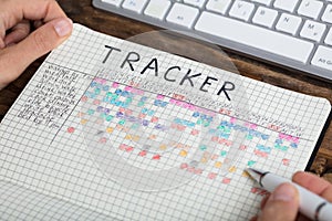 Person Drawing Tracker Chart On Notebook