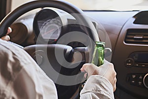 Person driving a car while holding a bottle of beer. Drunk diving, unsafe driving concept