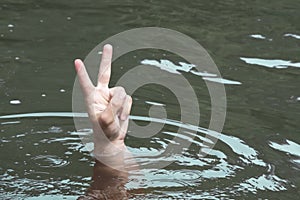 A person drowns in a river or lake and shows a symbol of victory and freedom. Male hand in the water with hand raised up. Winner