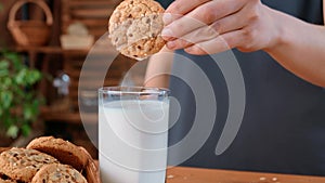 Person dunking cookies into fresh milk in glass, closeup view hand in kitchen, breakfast in morning