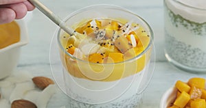 Person eating chia pudding with mango, yogurt and chia seeds. Creamy smoothie dessert, healthy raw dessert, closeup