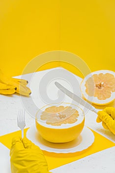 a person eating a grapefruit pomelo at the table, a room with yellow walls. human holding a knife and fork