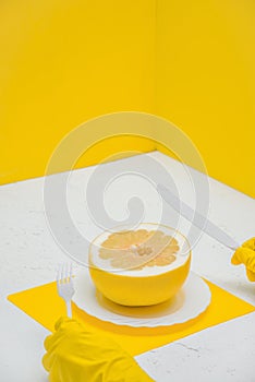 a person eating a grapefruit pomelo at the table, a room with yellow walls. human holding a knife and fork