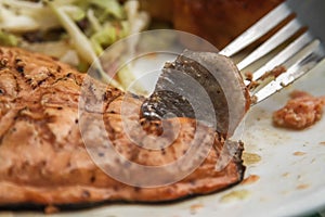 Person eating grilled salmon with pasta and salad on a plate