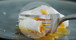 Person eating a poached egg with soft runny egg yolk with fork, close up slow motion video clip, boiled benedict egg on