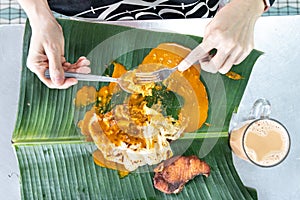 Person eating roti canai or paratha with curry on banana leaf with teh tarik or milk tea