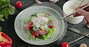 Person eating salad with fresh vegetables with stracciatella cheese on top, healthy salad with leaves and tomato