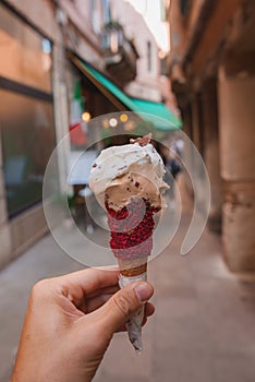 Person enjoying a red ice cream cone in a charming urban alleyway in Venice, Italy