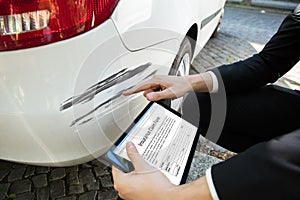 Person Examining Damaged Car While Filling Insurance Claim Form