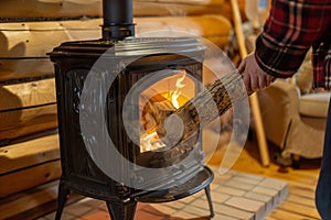 person feeding a log into a castiron stove in a log cabin interior