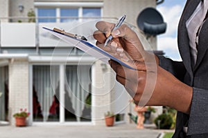 Person Filling Document In Front Of House