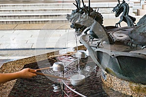 Person filling up ladle with water of chozuya fountain