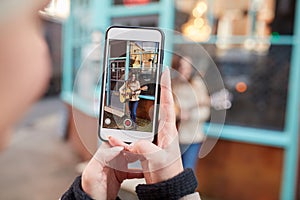 Person Filming Female Musician Busking Playing Acoustic Guitar And Singing To Crowd On Mobile Phone