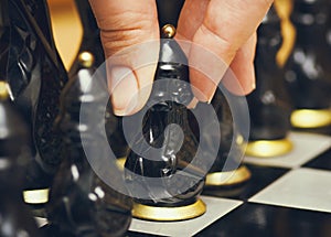 Person fingers with black pawn makes first move on chess board.