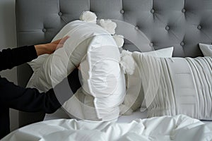 person fluffing pillows against a gray headboard