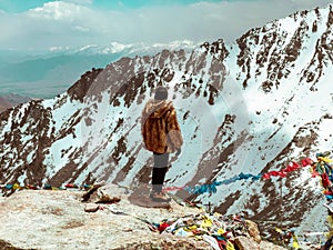 Person in a fur coat standing on the edge of a cliff and looking at Himalayas. Khardung La, India. photo